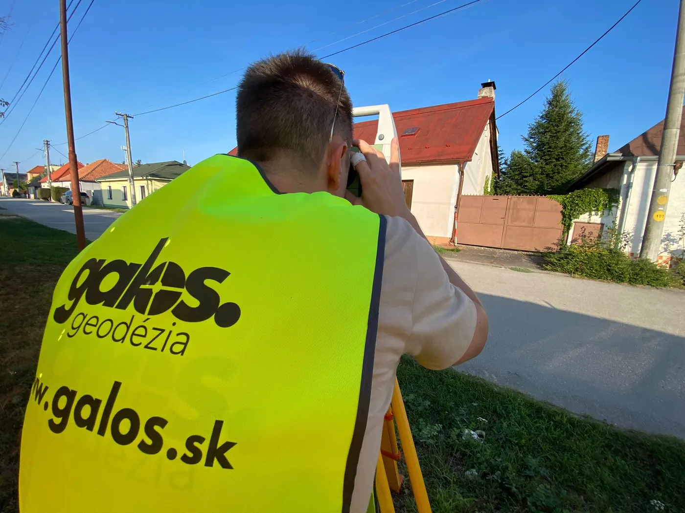 Geodet Galos v reflexnej veste pri meraní nivelačným prístrojom